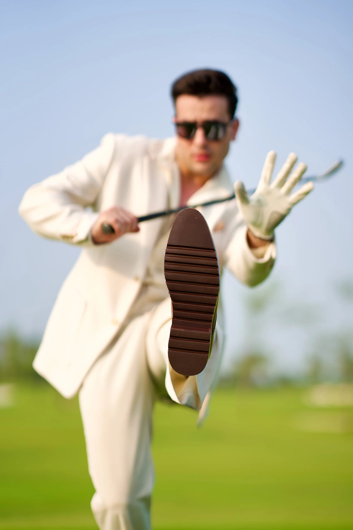 A client in a cream suit kicks up the sole of his Cueřo shoe toward the camera on a golf course