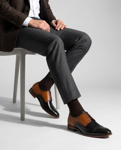 Askari two-tone leather brogues styled with formal outfit in seated model pose showcasing crafted luxury menswear elegance
