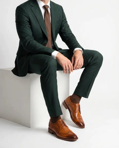 Man wearing a dark green suit with a brown tie and shoes