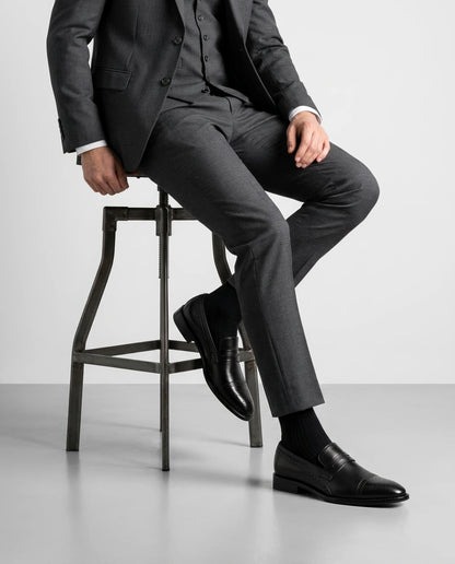 Deyoshi black leather loafers styled with grey suit in seated model pose showcasing luxury formal menswear elegance
