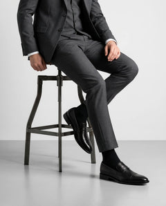 Deyoshi black leather loafers styled with grey suit in seated model pose showcasing luxury formal menswear elegance