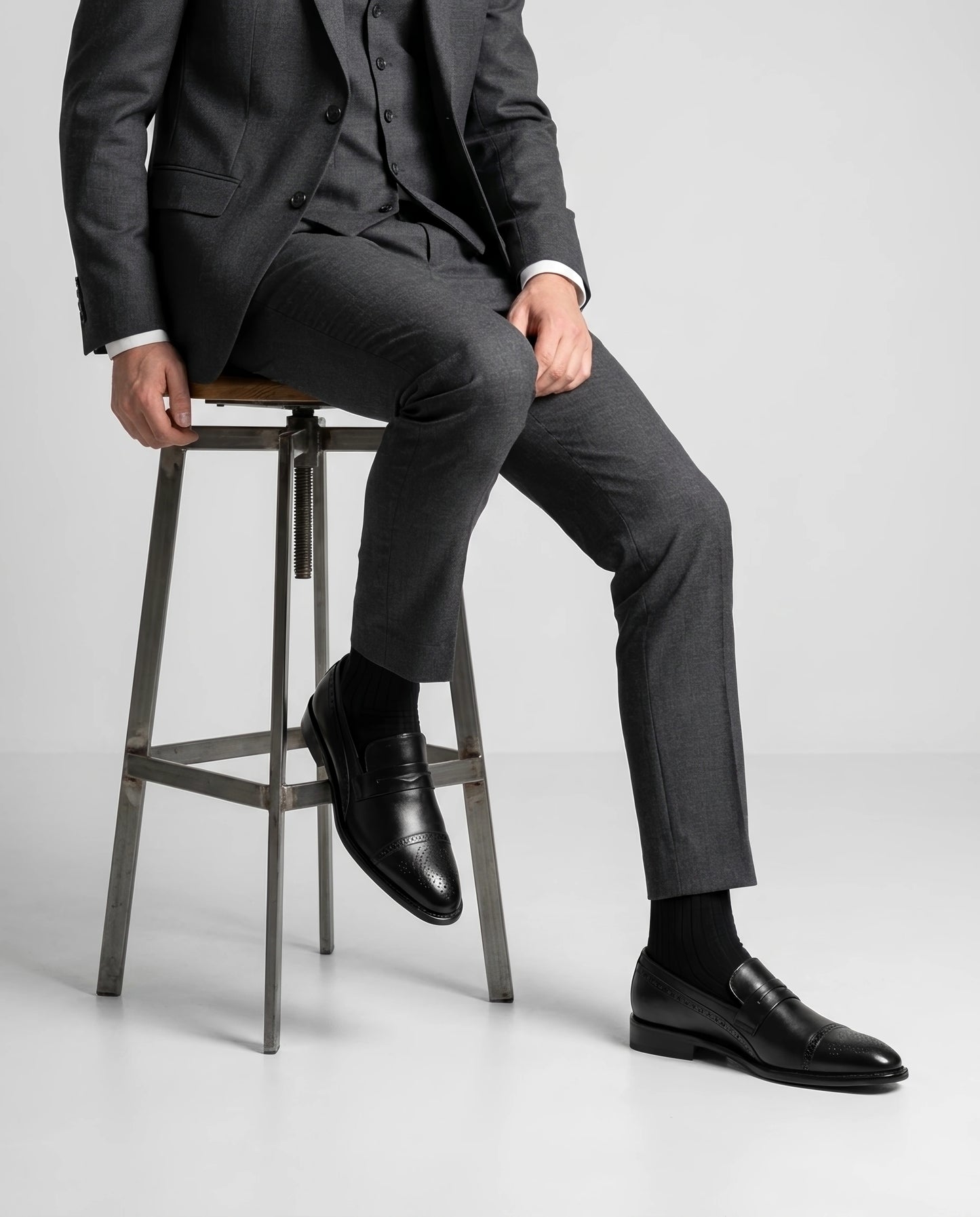 Deyoshi black leather loafers worn with grey suit in seated editorial pose highlighting refined craftsmanship and timeless formal style