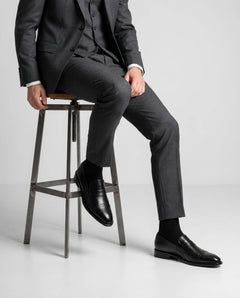 Deyoshi black leather loafers worn with grey suit in seated editorial pose highlighting refined craftsmanship and timeless formal style