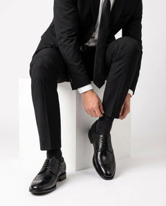 Huxley black lace-up formal shoes styled with black suit in seated model pose showcasing luxury formal menswear elegance