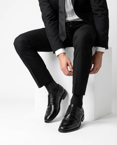 Huxley black lace-up formal shoes styled with black suit in seated editorial pose highlighting timeless sophistication and premium craftsmanship