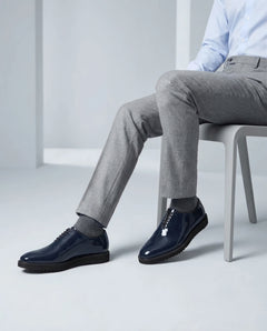 Lucifer Cueřo Grand Atelier navy blue patent leather formal dress shoes worn with grey trousers in a seated studio fashion pose showcasing luxury shine and premium finish