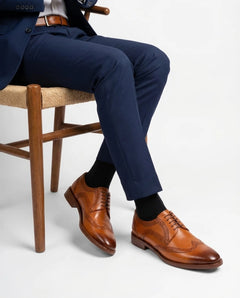 Shelby brogue formal lace-up shoes styled with blue suit in seated model pose highlighting refined craftsmanship and modern gentleman aesthetic